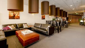 Un hall d’hôtel moderne avec des canapés en cuir, un pouf rouge et un espace repas comprenant des tables et des chaises.