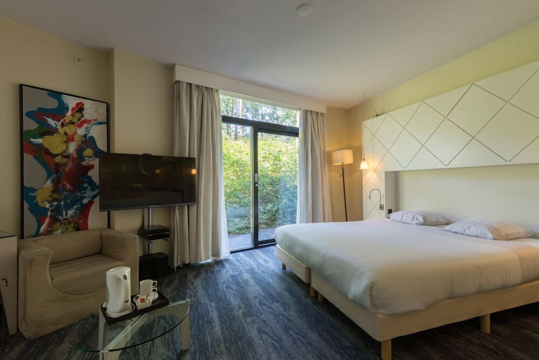 Een hotelkamer met een bed, een televisie, een bank, een salontafel en een schilderij.