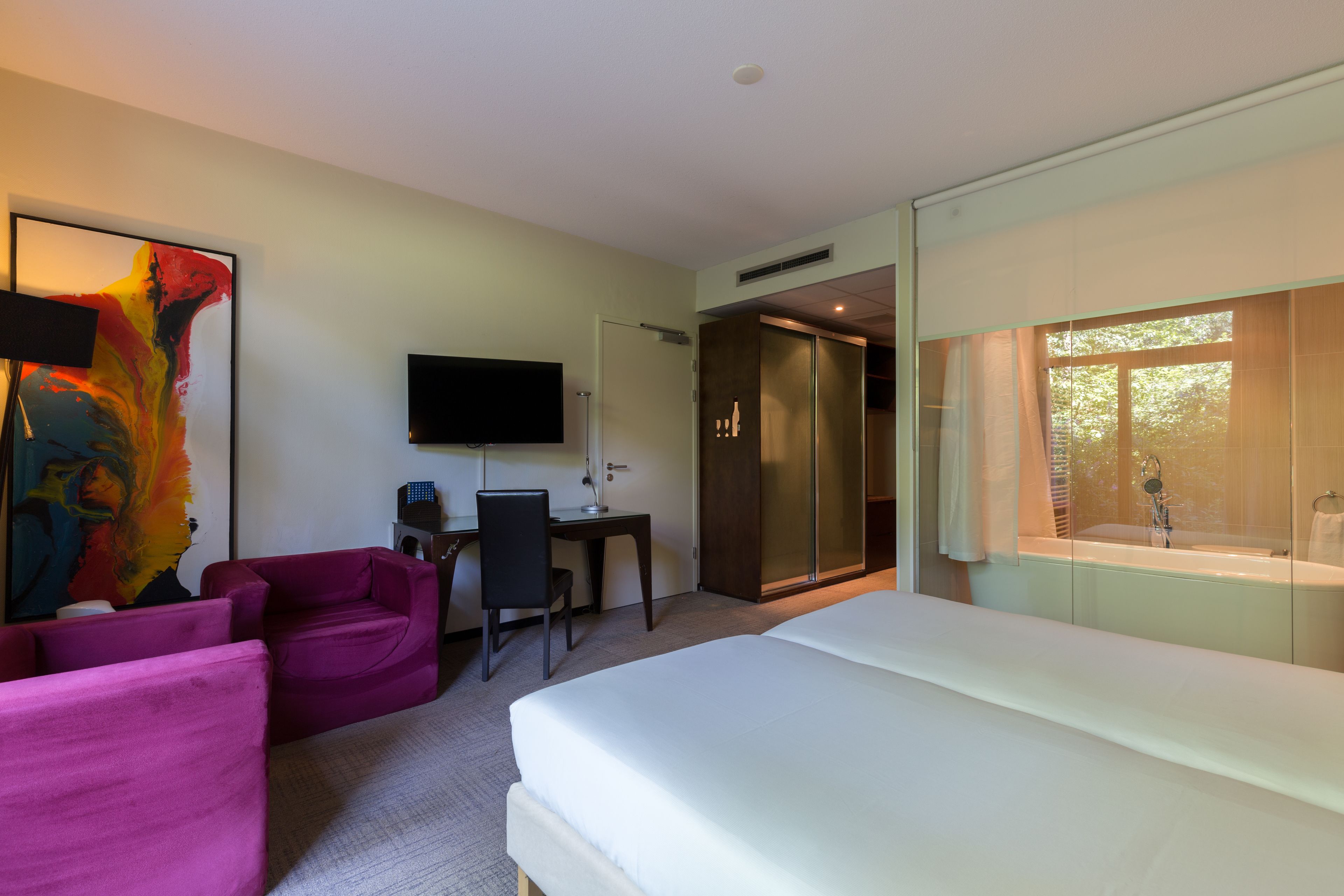 Habitación de hotel con cama, escritorio, silla, televisor y zona de ducha.