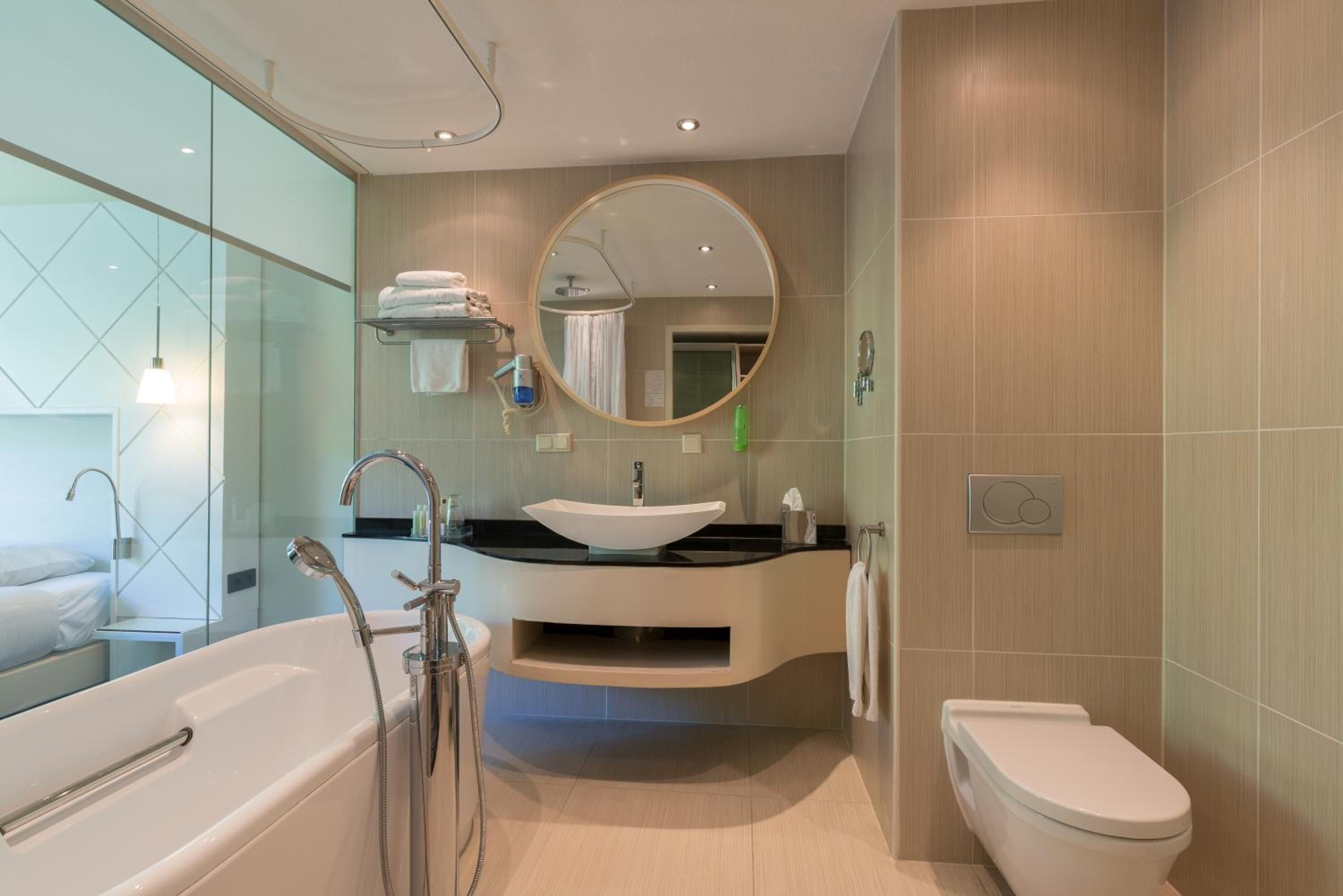 Un baño moderno con una bañera independiente, un tocador con lavamanos, inodoro y un espejo grande.