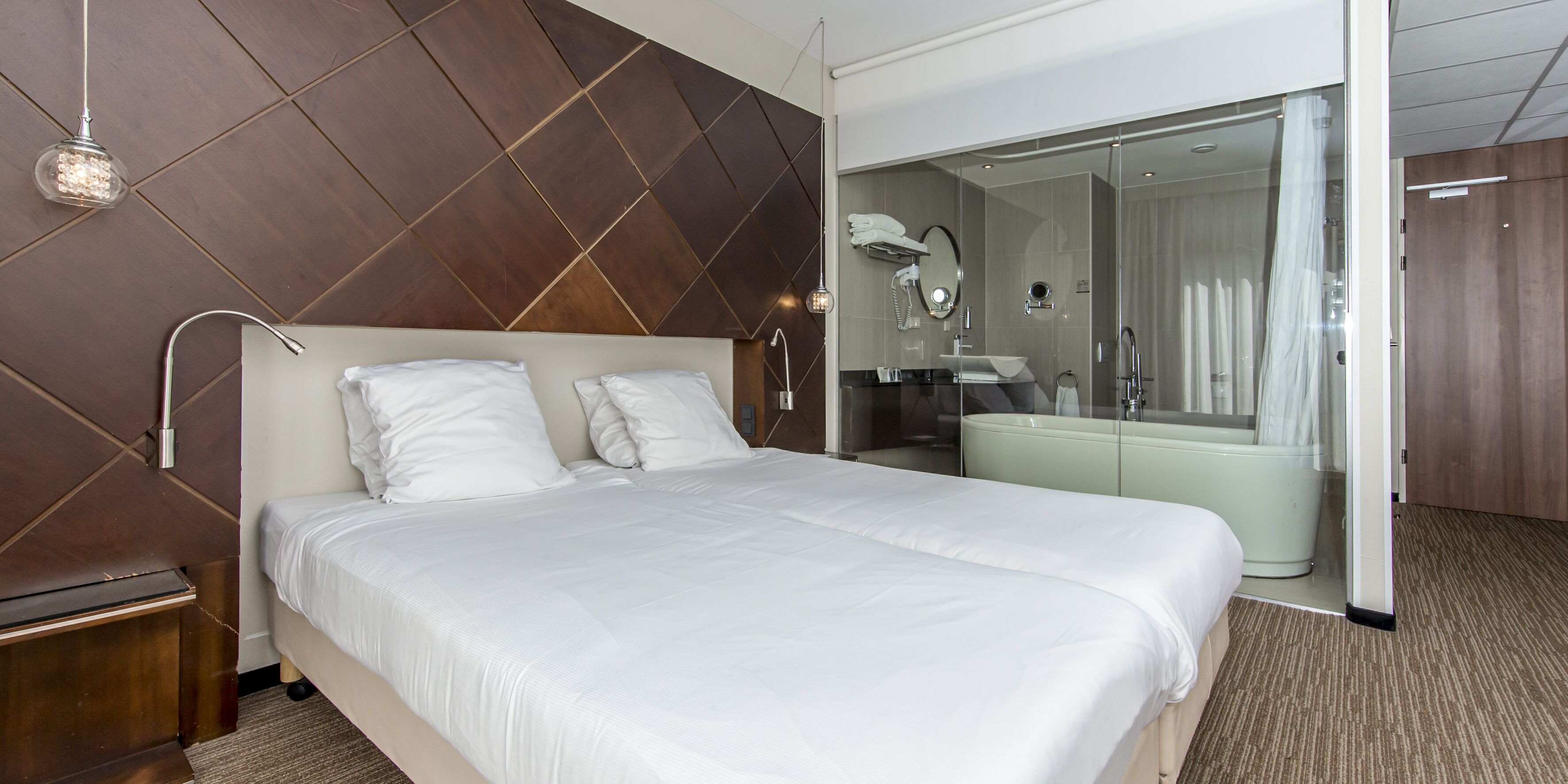 A modern hotel room with a large bed, a walk-in closet, and a separate bathroom with a bathtub.