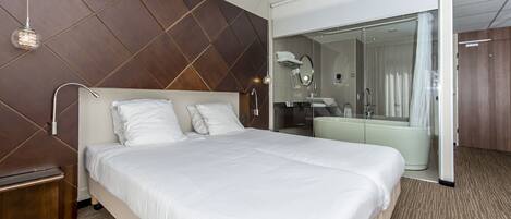 A modern hotel room with a large bed, a walk-in closet, and a separate bathroom with a bathtub.