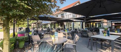 An outdoor café with tables and chairs, umbrellas, and potted plants.