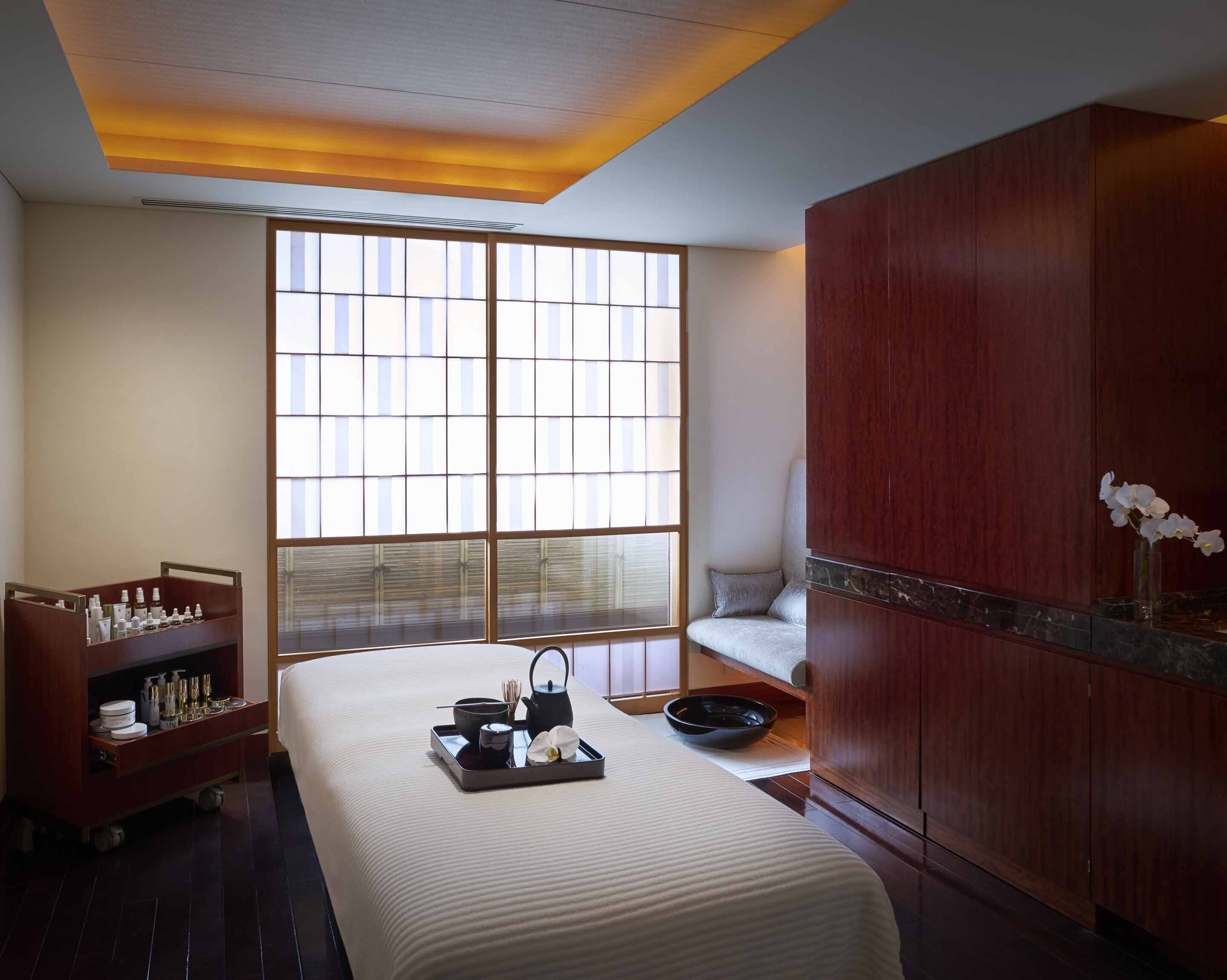 A hotel room with a large window, a bed with a tray of amenities, a wooden cabinet, and a small seating area.
