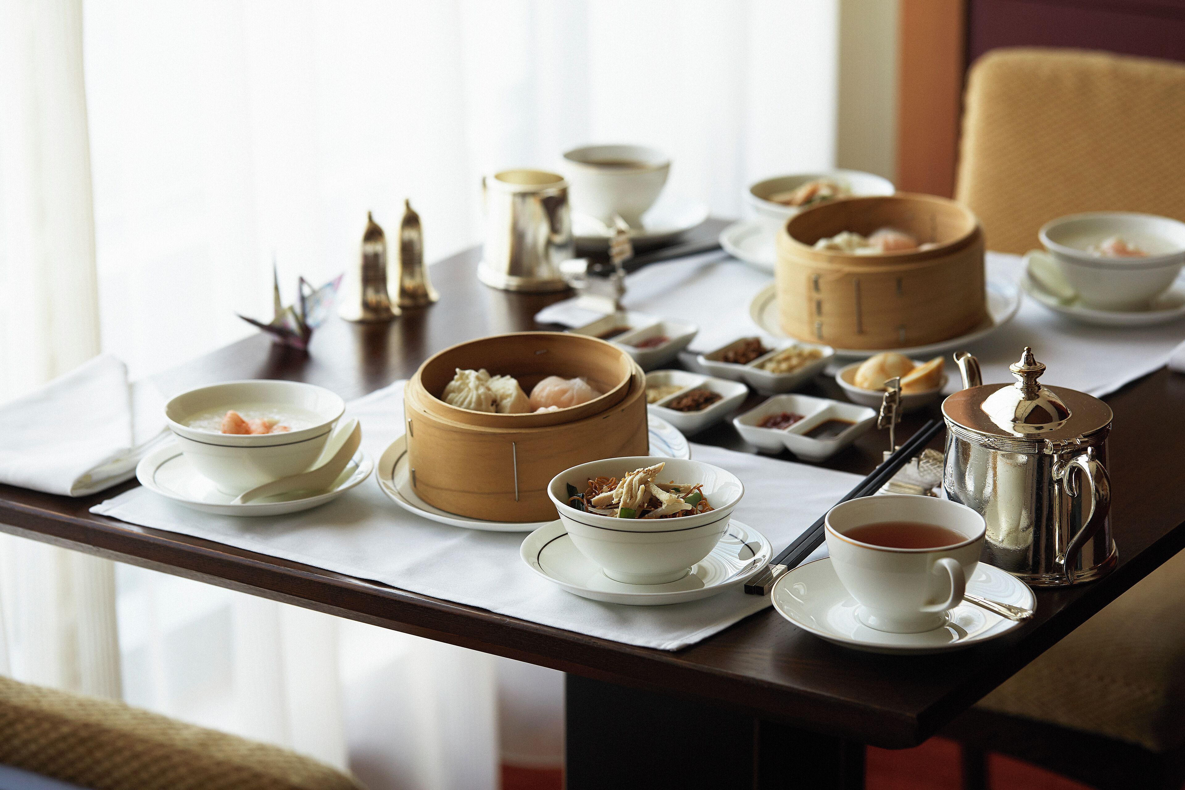 Une table à manger avec divers plats, notamment des dim sum, du thé et une théière.