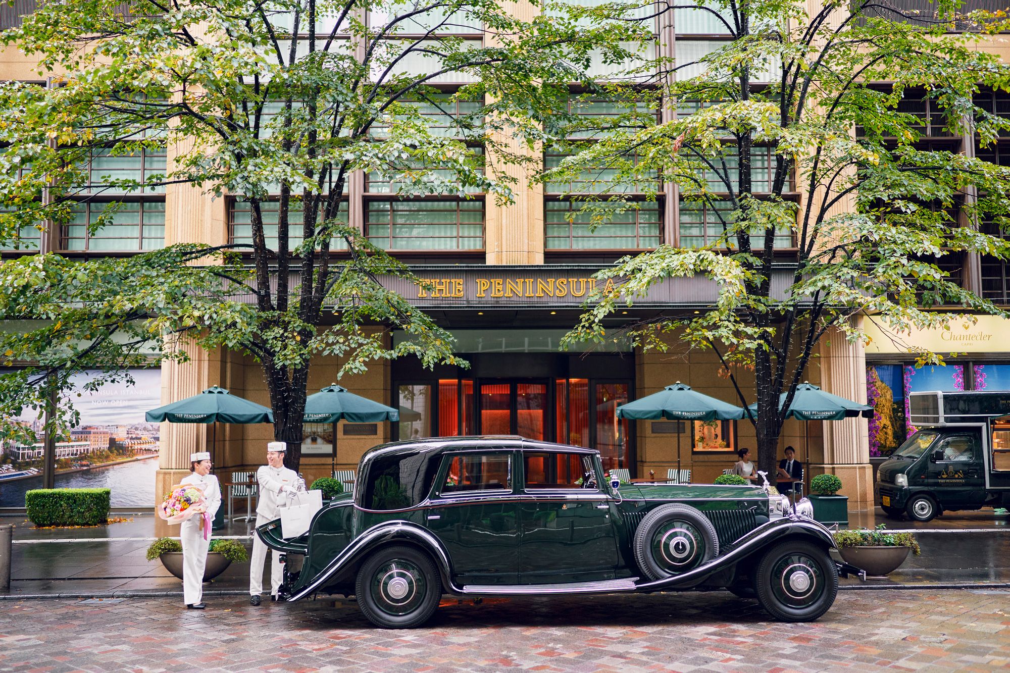 A vintage green car parked in front of a building with a sign reading 'THE PENINSULA'.