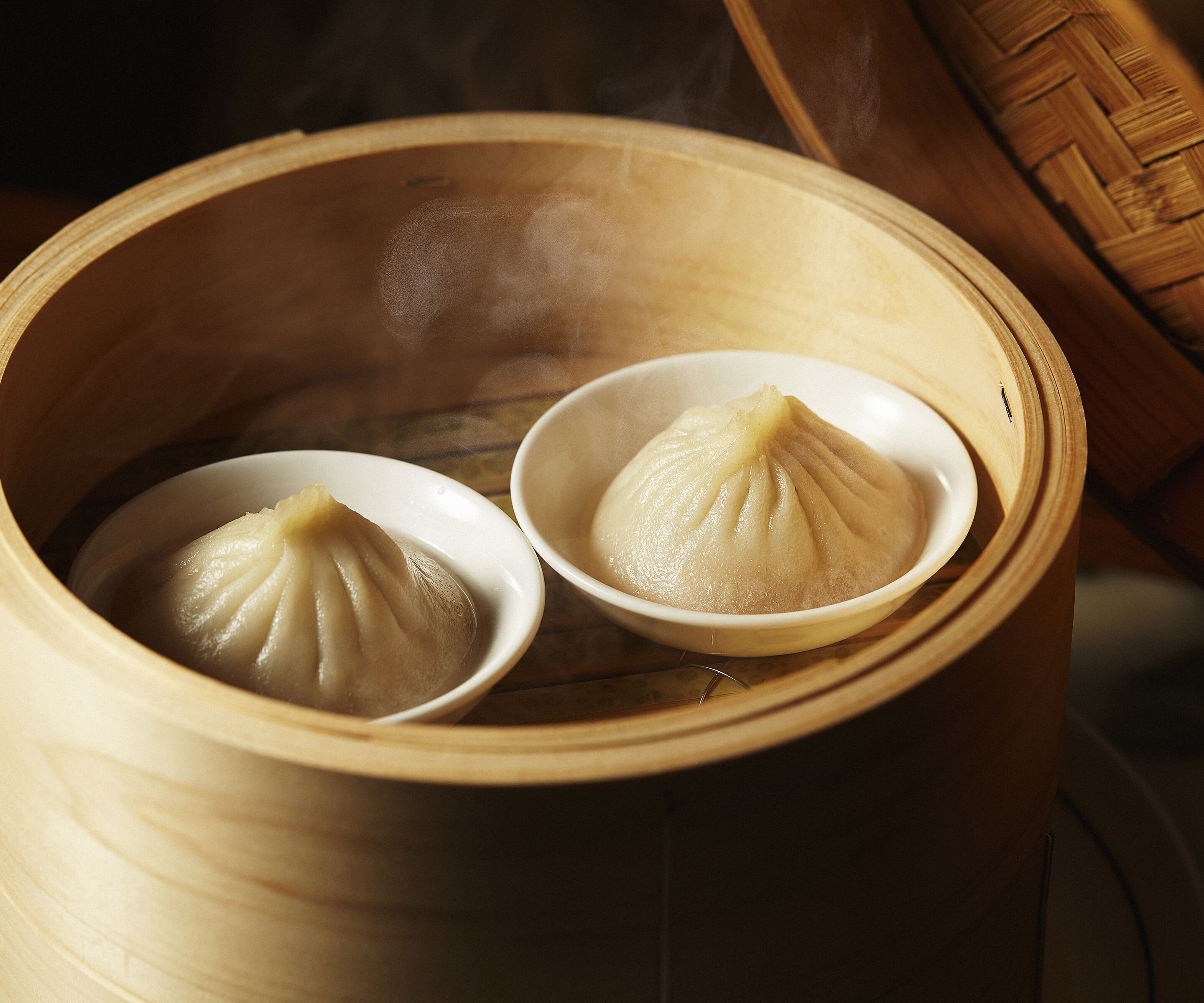Two white bowls of steamed dumplings in a bamboo steamer.