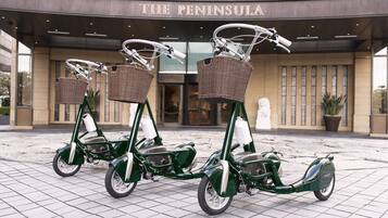 Dos bicicletas verdes con cestas estacionadas frente a un edificio con un letrero que dice 'The Peninsula'.