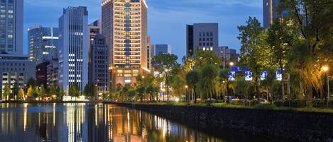 A cityscape with modern buildings, a calm river reflecting the structures, and a well-lit urban environment.