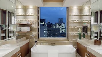 A modern bathroom with a large bathtub, dual sinks, and a city view.