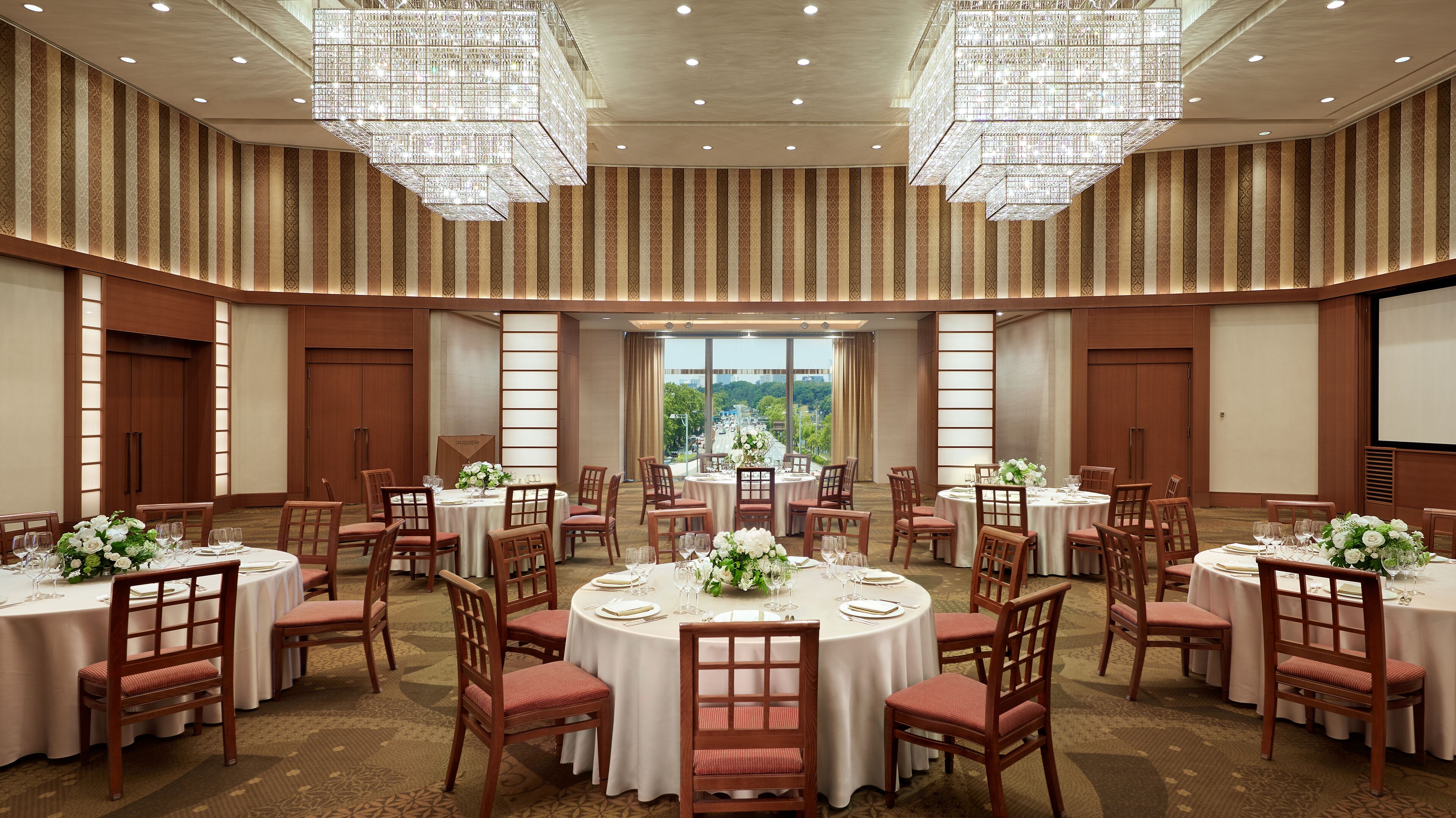 A conference room with multiple round tables, each set with white tablecloths, chairs, and floral centerpieces.