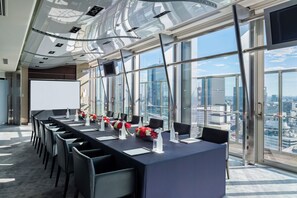 A modern conference room with a long table, chairs, and a city view through large windows.