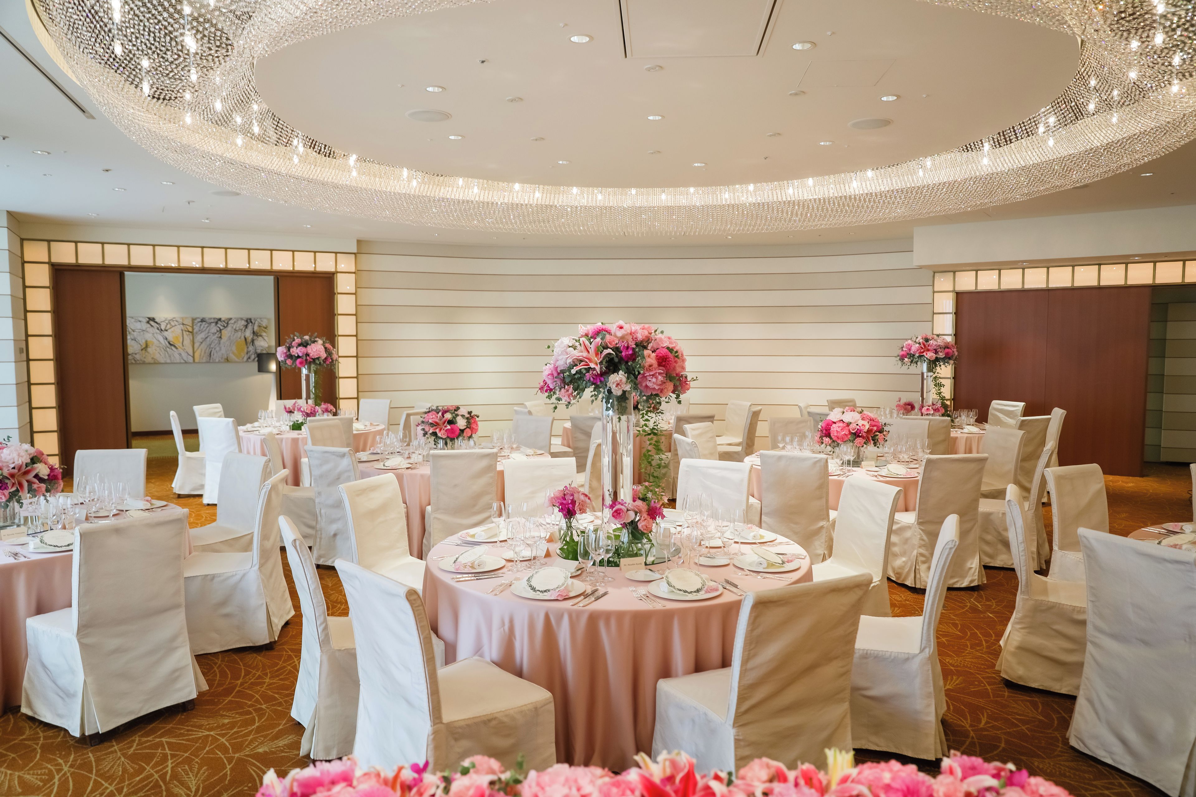 Un salón de banquetes con mesas redondas, sillas blancas y centros de mesa florales.