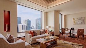 A modern hotel room with a large window offering a city view, a cozy seating area with a sofa and chairs, a small dining table, and a decorative vase. - The Peninsula Tokyo (Tokyo)