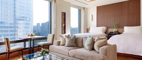 A hotel room with a large bed, a sofa, a small table, and a view of the city.