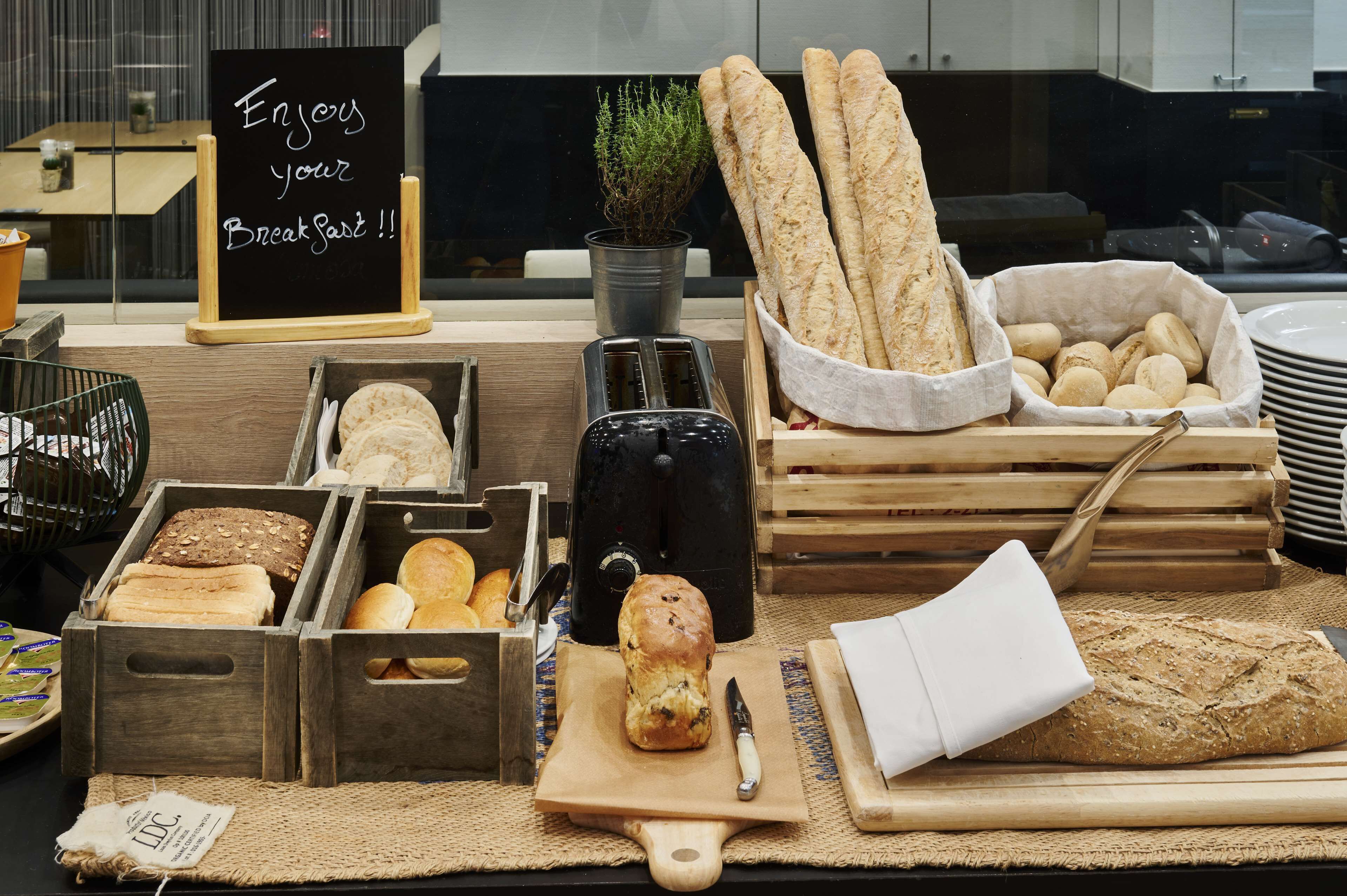 A breakfast buffet with various breads, pastries, and a sign encouraging guests to enjoy their breakfast.
