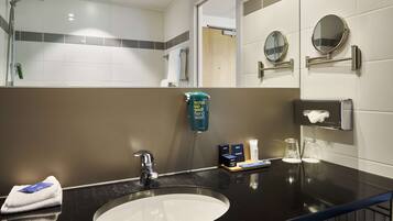 A hotel bathroom with a sink, mirror, towel dispenser, and hand soap dispenser.