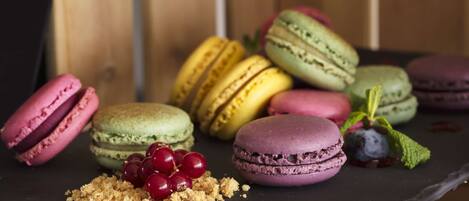 Erilaisia värikkäitä macaron-leivoksia on aseteltu riviin liuskelevylle, ja taustalla on maalaishenkinen puinen pinta.