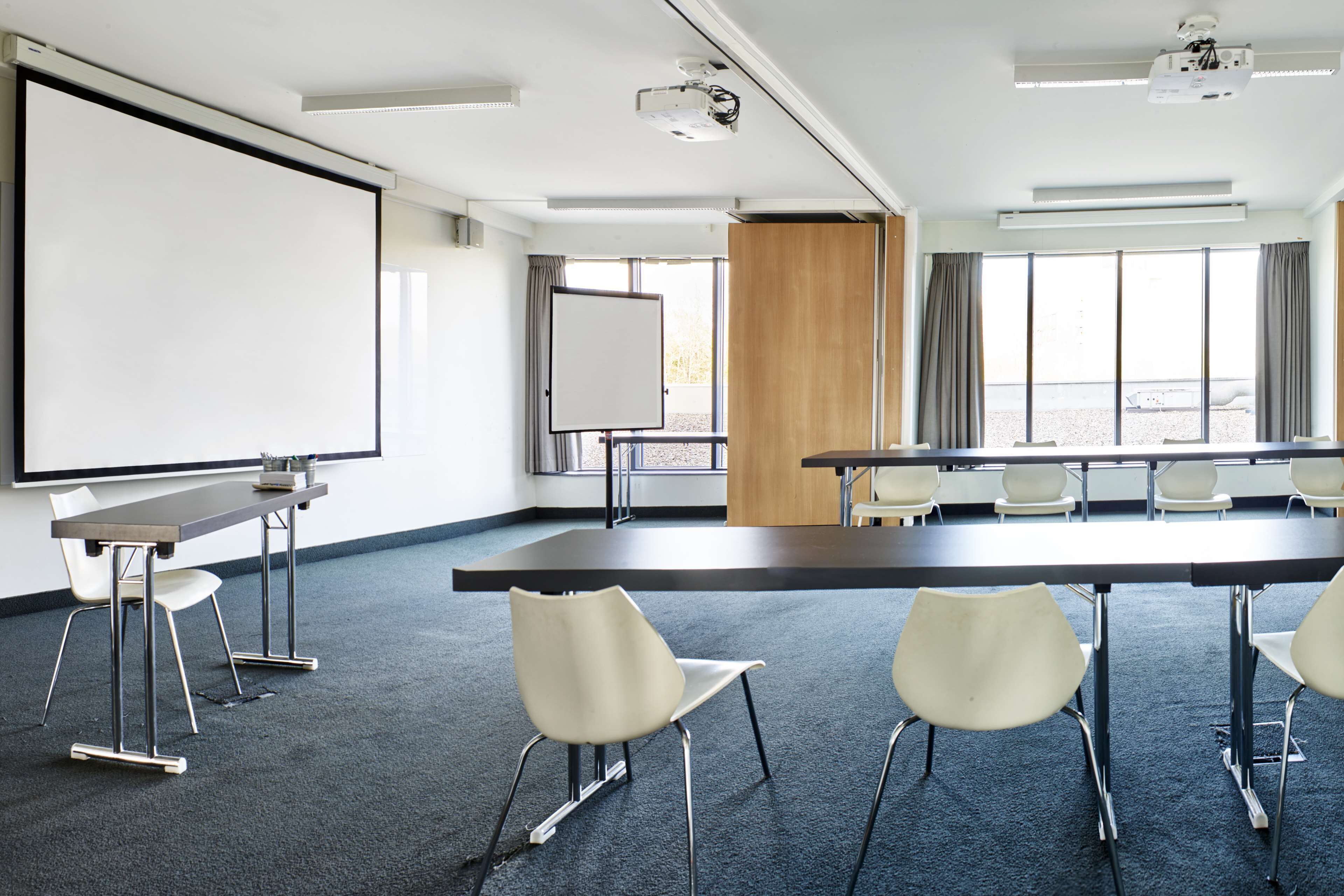 Una sala de conferencias con una gran mesa, sillas, una pizarra y un proyector.