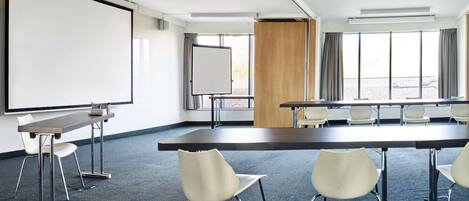 Una sala de conferencias con una gran mesa, sillas, una pizarra y un proyector.