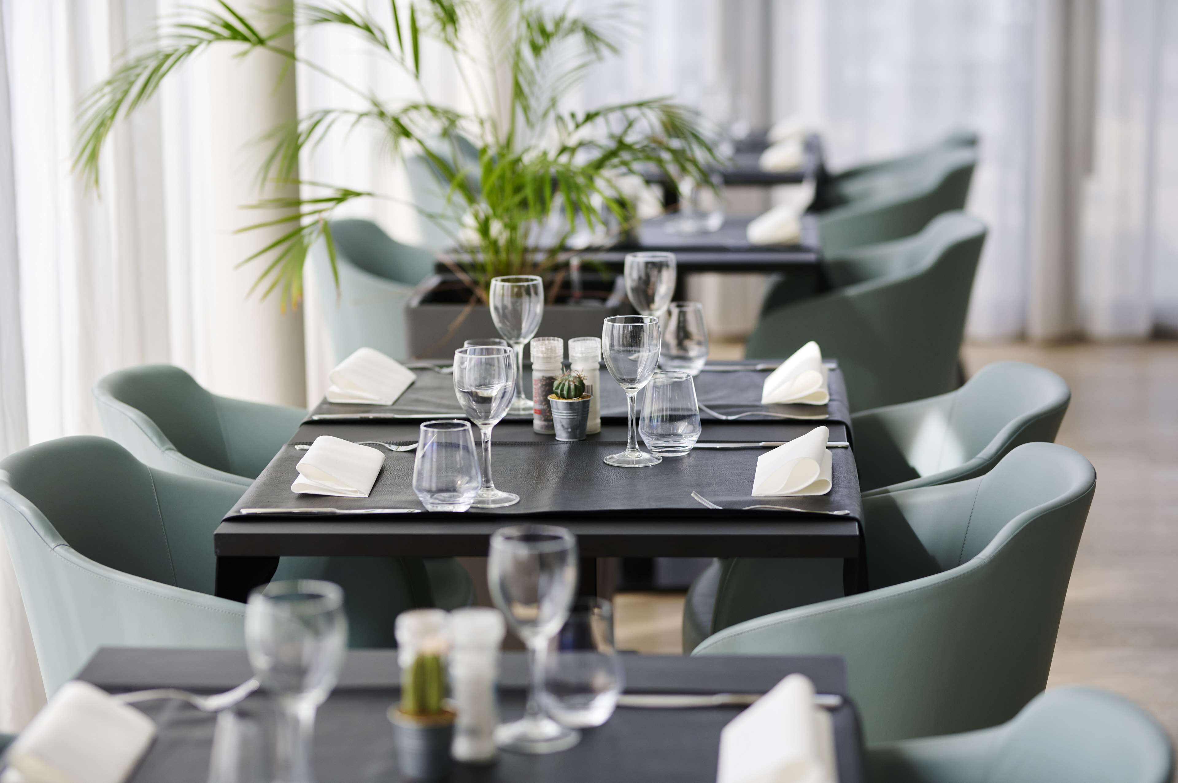 Een eetruimte met gedekte tafels, met groene bekleden stoelen en glazen servies.