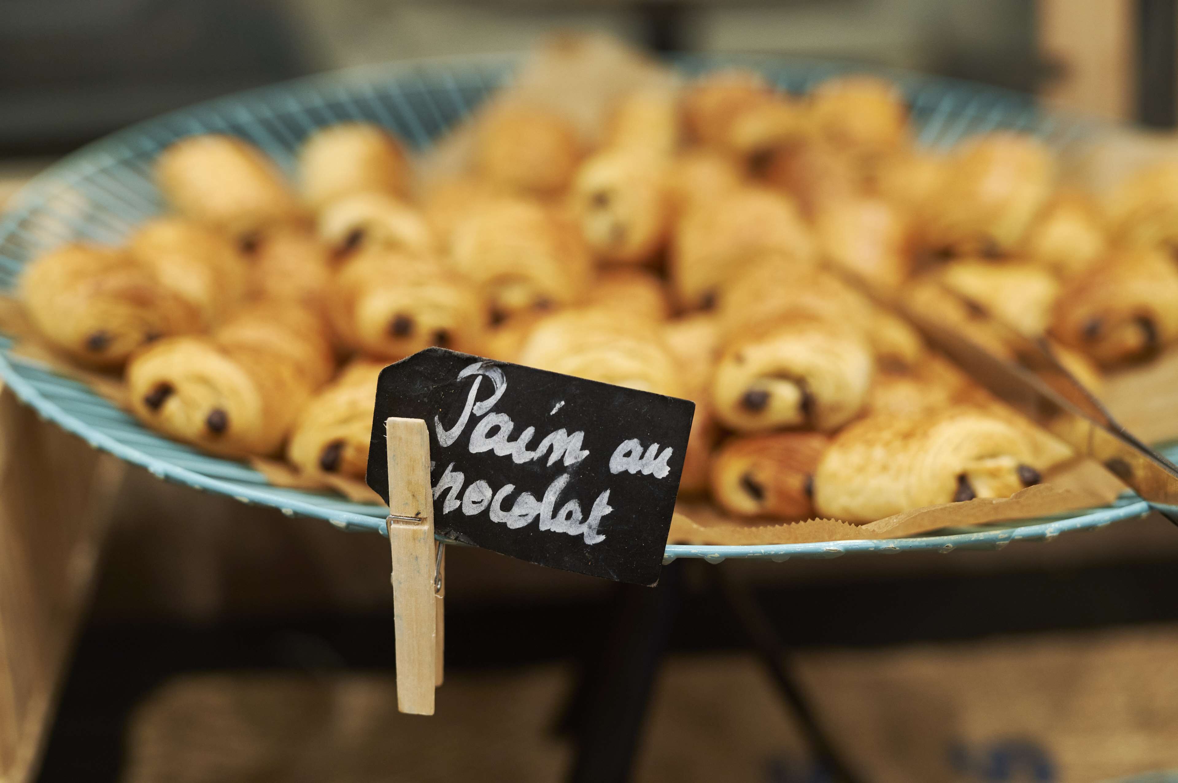 Un plateau de viennoiseries étiqueté « Pain au chocolat », maintenu par une pince en bois sur laquelle est fixé un petit panneau.