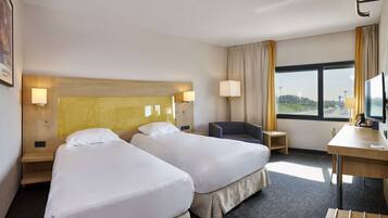 A hotel room with two beds, a desk, a chair, a TV, and a window with a view.