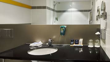 A hotel bathroom with a black sink, a mirror, a handheld showerhead, and a towel rack.