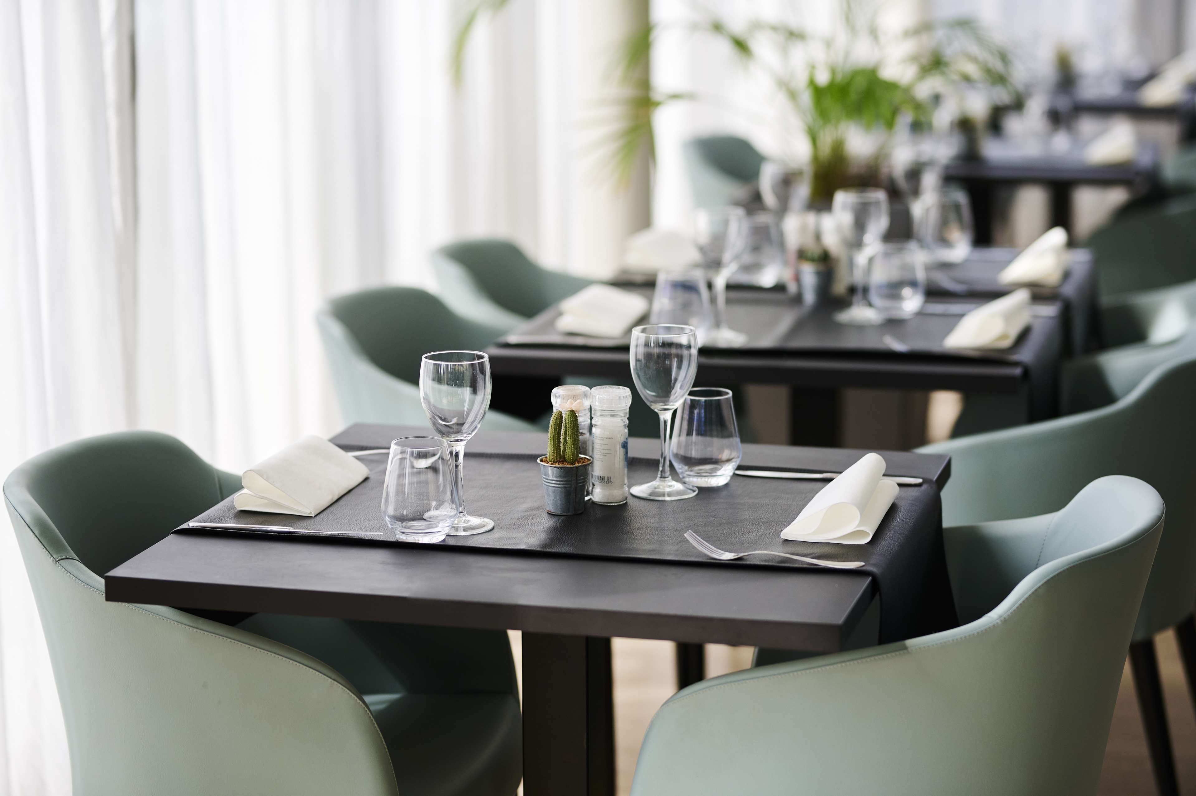 Un ambiente de restaurante con mesas dispuestas para comer, con sillas verdes y vajilla ordenada.