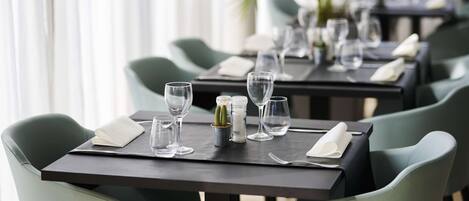 Un ambiente de restaurante con mesas dispuestas para comer, con sillas verdes y vajilla ordenada.