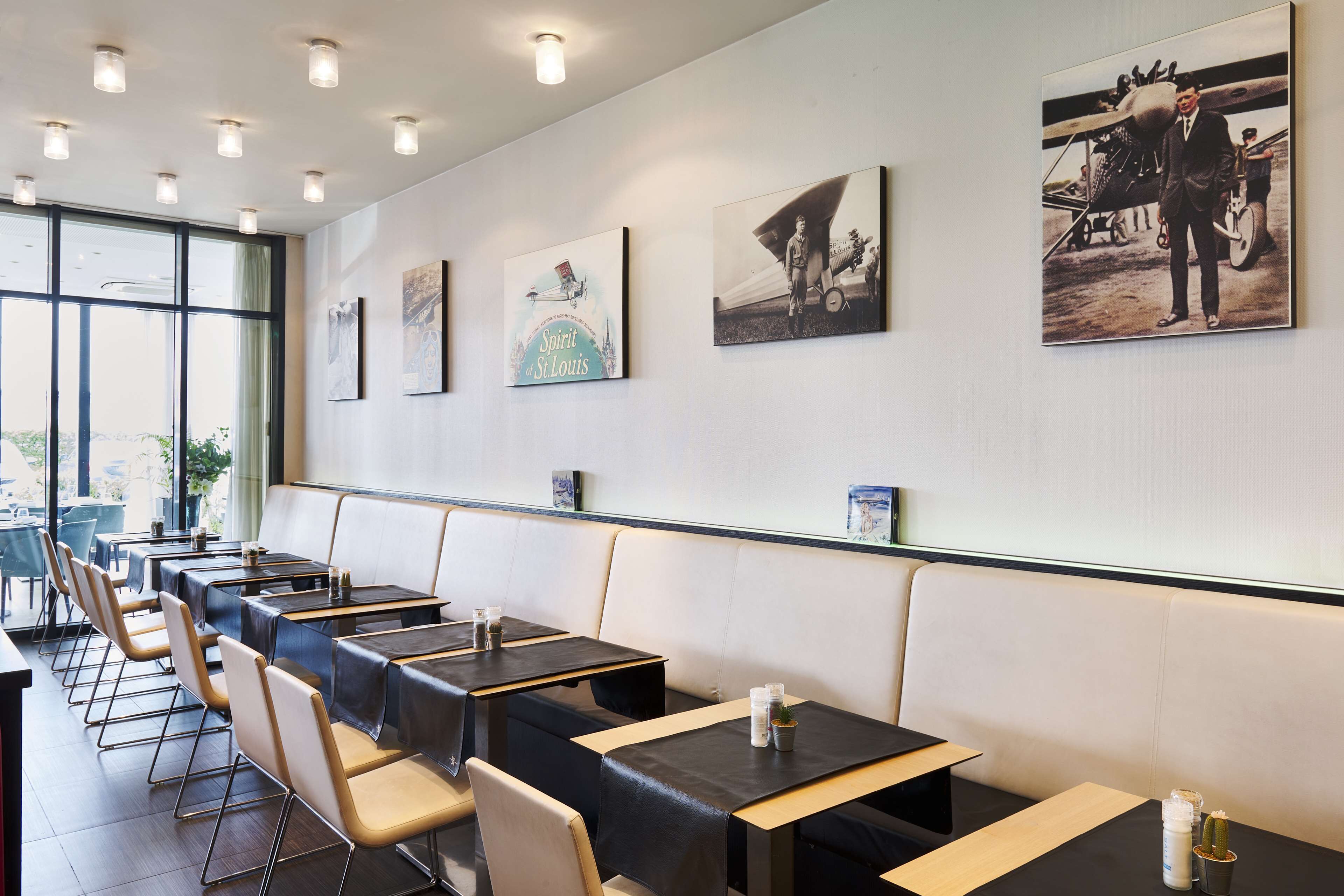 Un restaurante con mesas largas y cabinas, cuadros en la pared y vistas amplias a través de grandes ventanales.