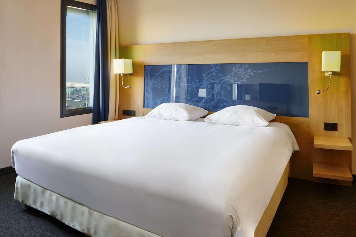 A hotel room with a large bed, two bedside lamps, a nightstand, and a window with curtains.