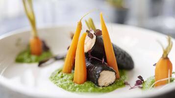 A plate of food with a green sauce base, topped with carrot sticks and a dark, round item, possibly a vegetable or meat.