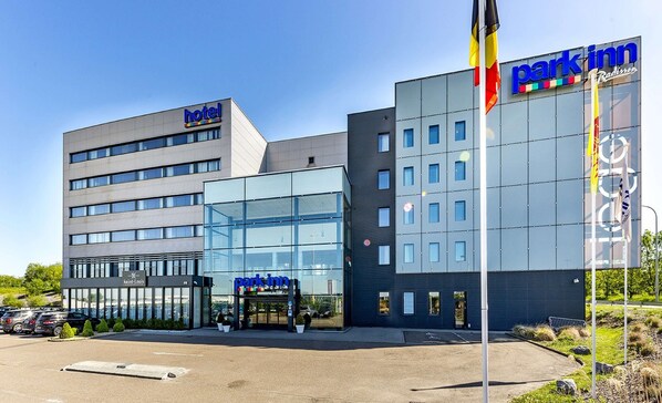 A hotel with a modern glass facade, a visible entrance, and a parking lot. - Park Inn by Radisson Liege Airport (Grace-Hollogne)