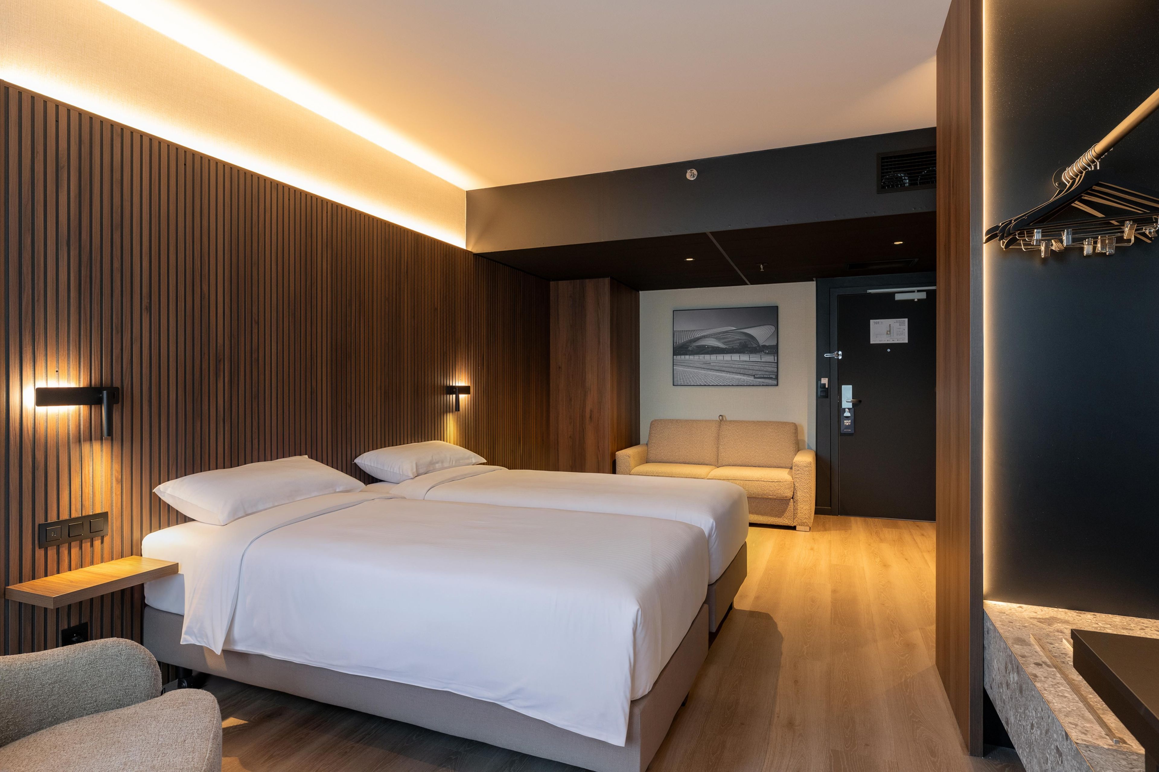 Une chambre d’hôtel moderne avec un grand lit, un coin salon et une vue sur un immeuble par la fenêtre.