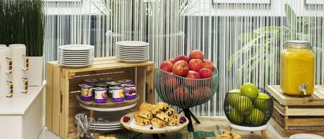 En morgenmadsbuffet med tallerkener med bagværk, en skål med æbler og en safthane.