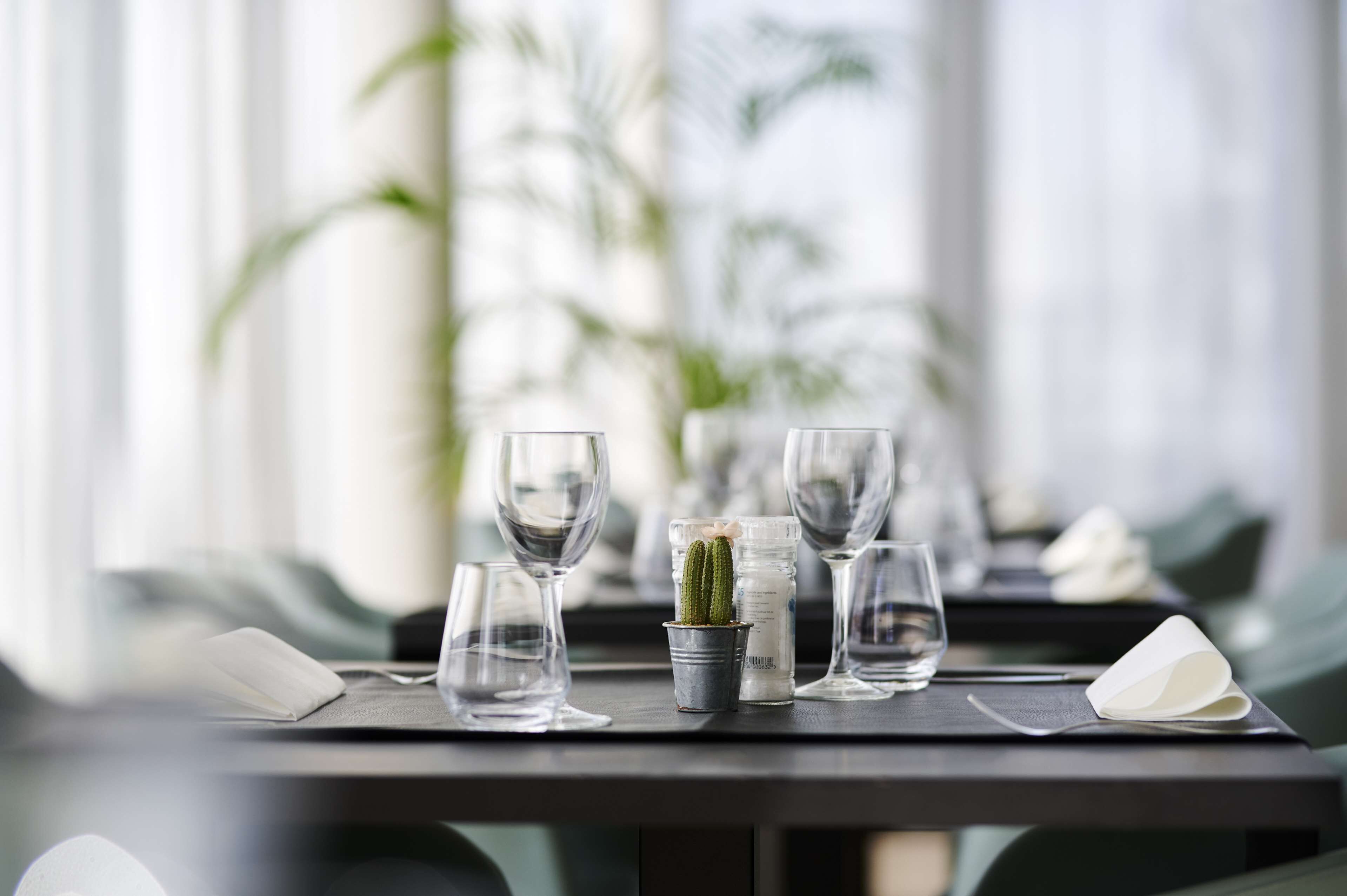 A dining table set with wine glasses, a cactus, and a water bottle.