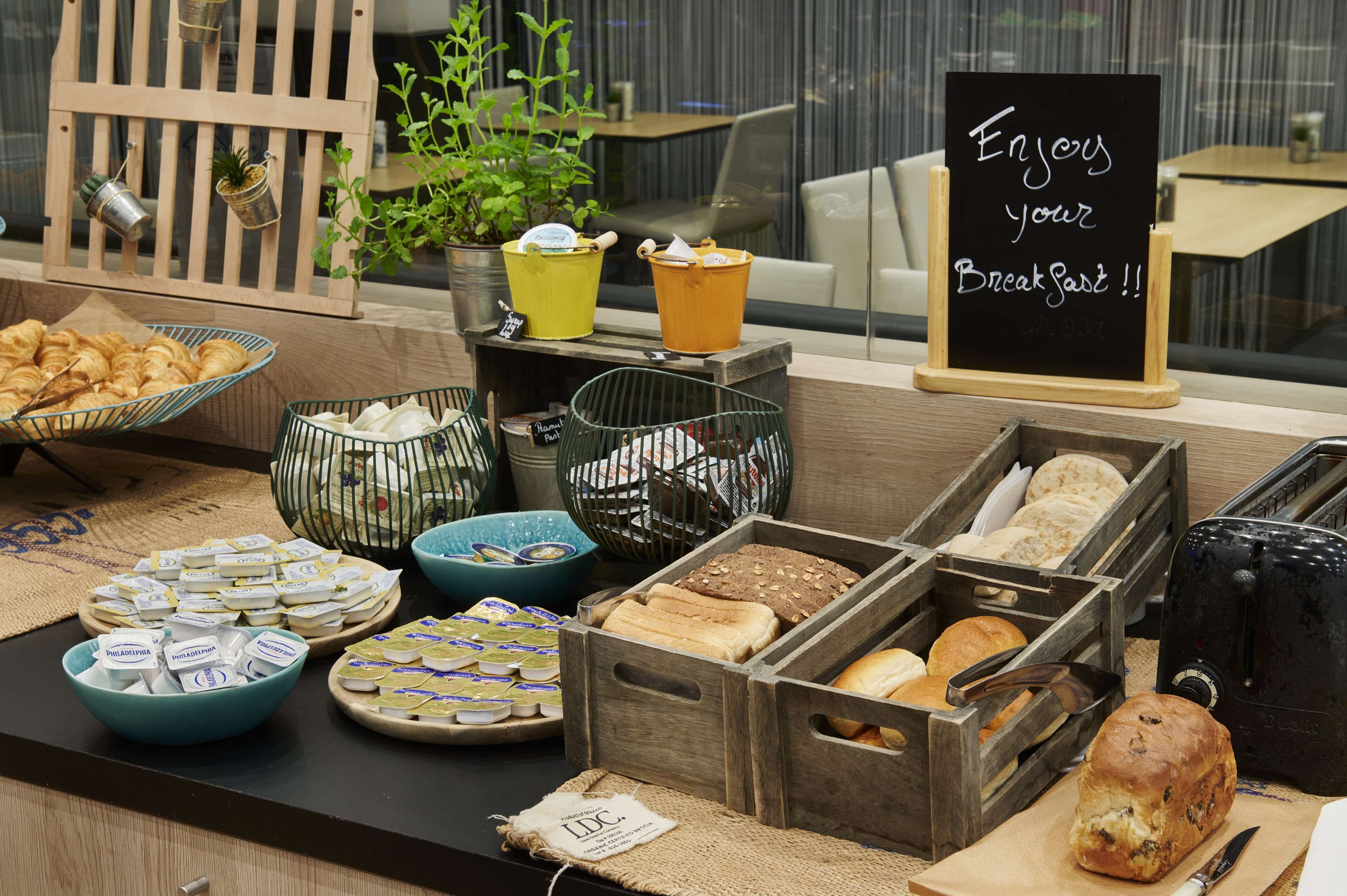 Um buffet de café da manhã com diversos alimentos e um aviso que diz 'Aproveite o seu café da manhã!!'.