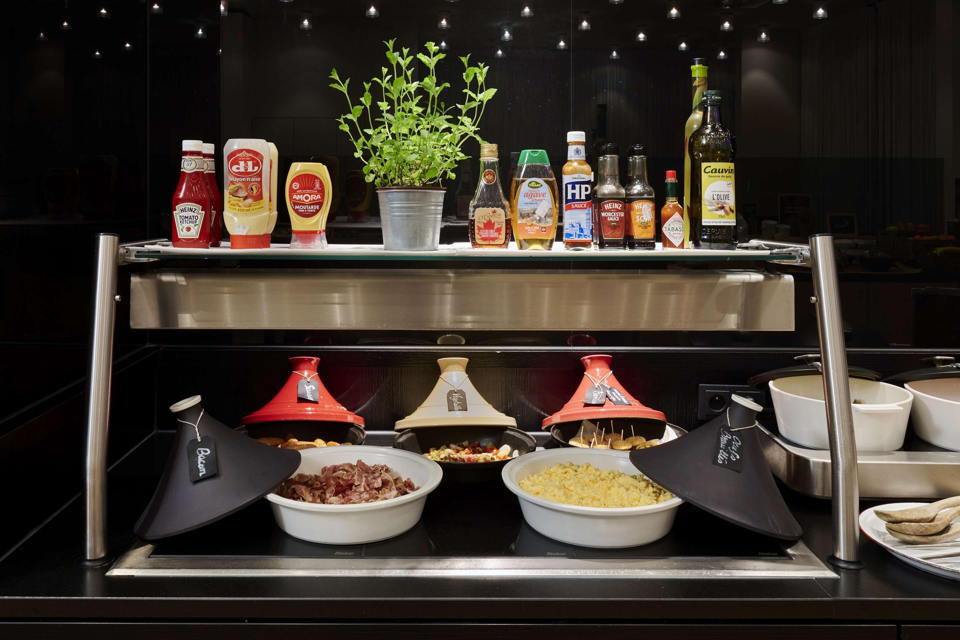 A buffet setup with various condiments, a potted plant, and covered dishes of food.