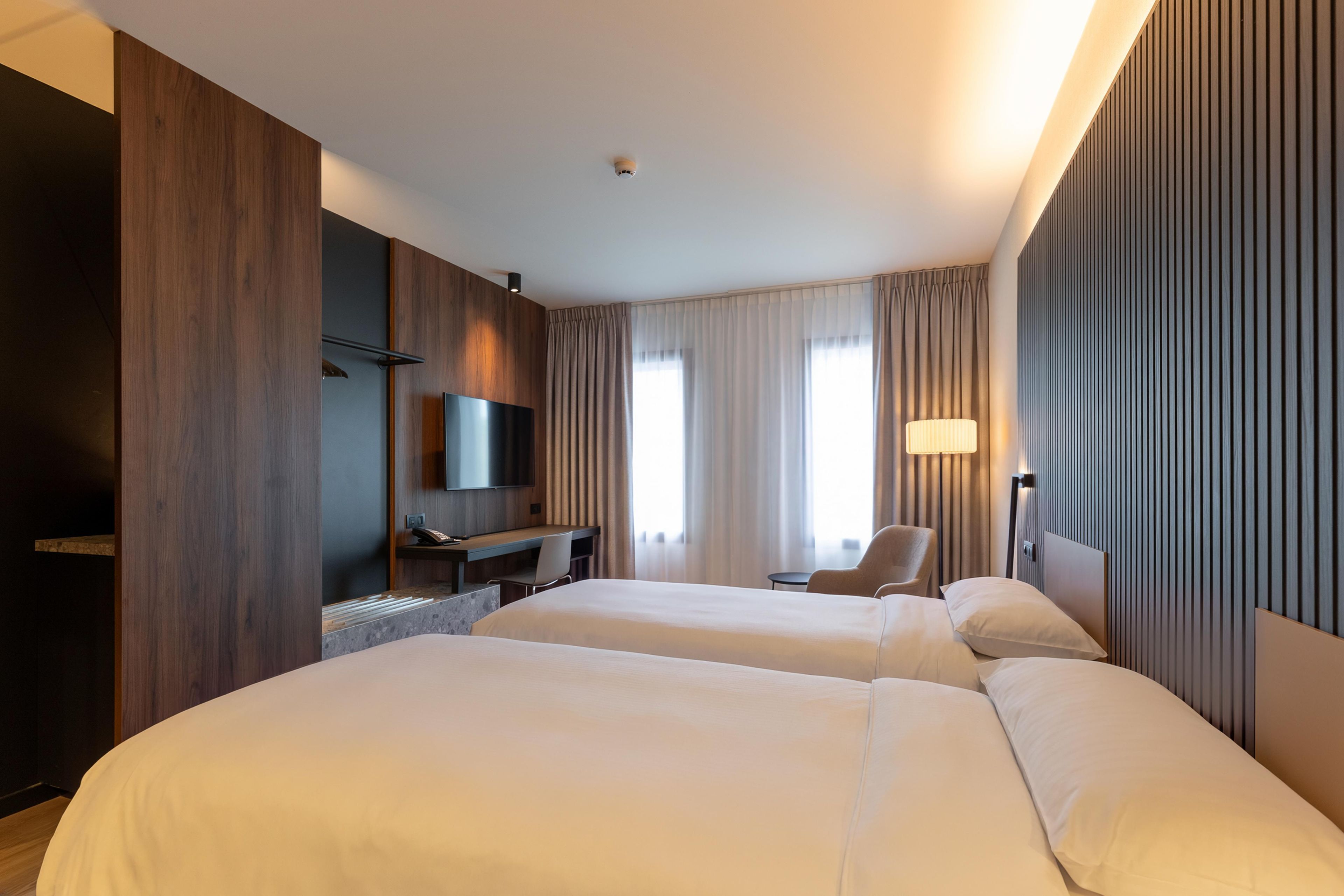 Una habitación de hotel con dos camas, un escritorio, una silla, un televisor y una lámpara.