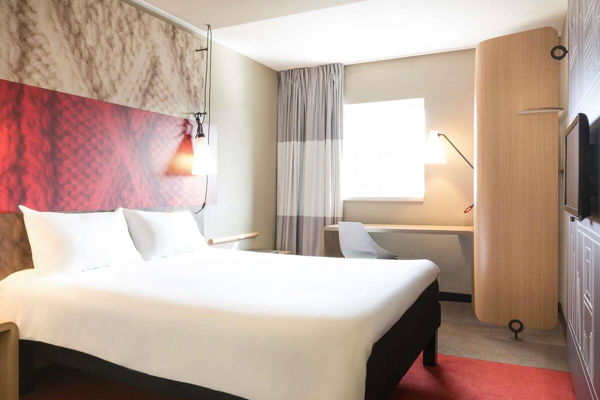 Een hotelkamer met een groot bed, een bureau, een stoel, een televisie en een raam met gordijnen.