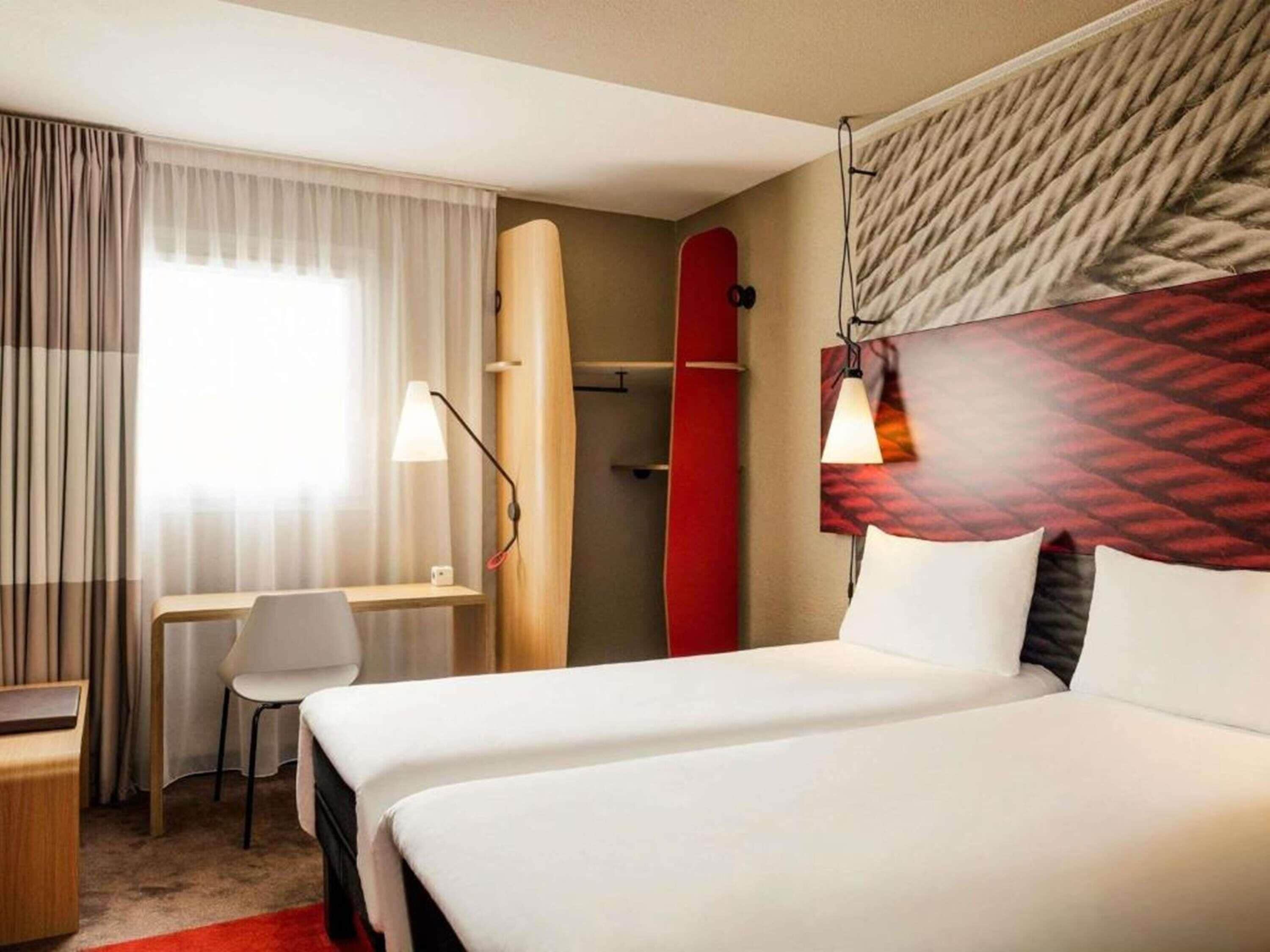 Hotelkamer met een bed, bureau, stoel, een surfplank en een wandlamp.