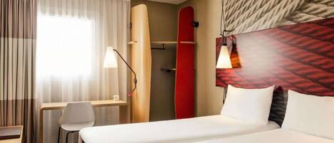 Hotelkamer met een bed, bureau, stoel, een surfplank en een wandlamp.
