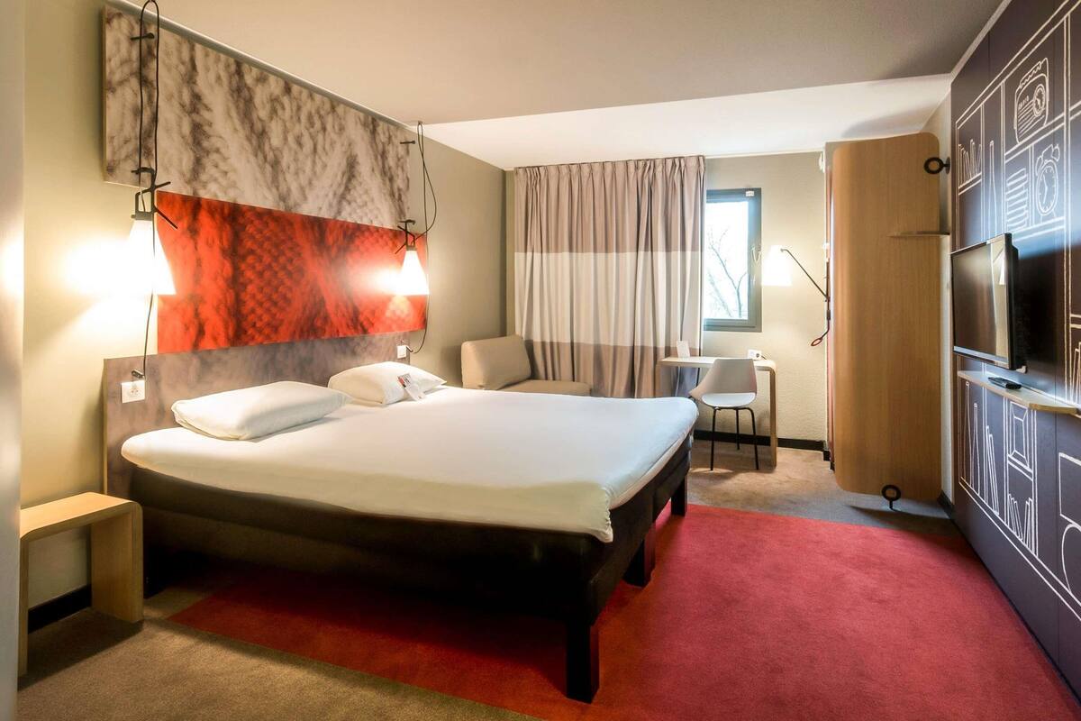 Een hotelkamer met een groot bed, een bureau met stoel, een televisie en een raam met gordijnen.
