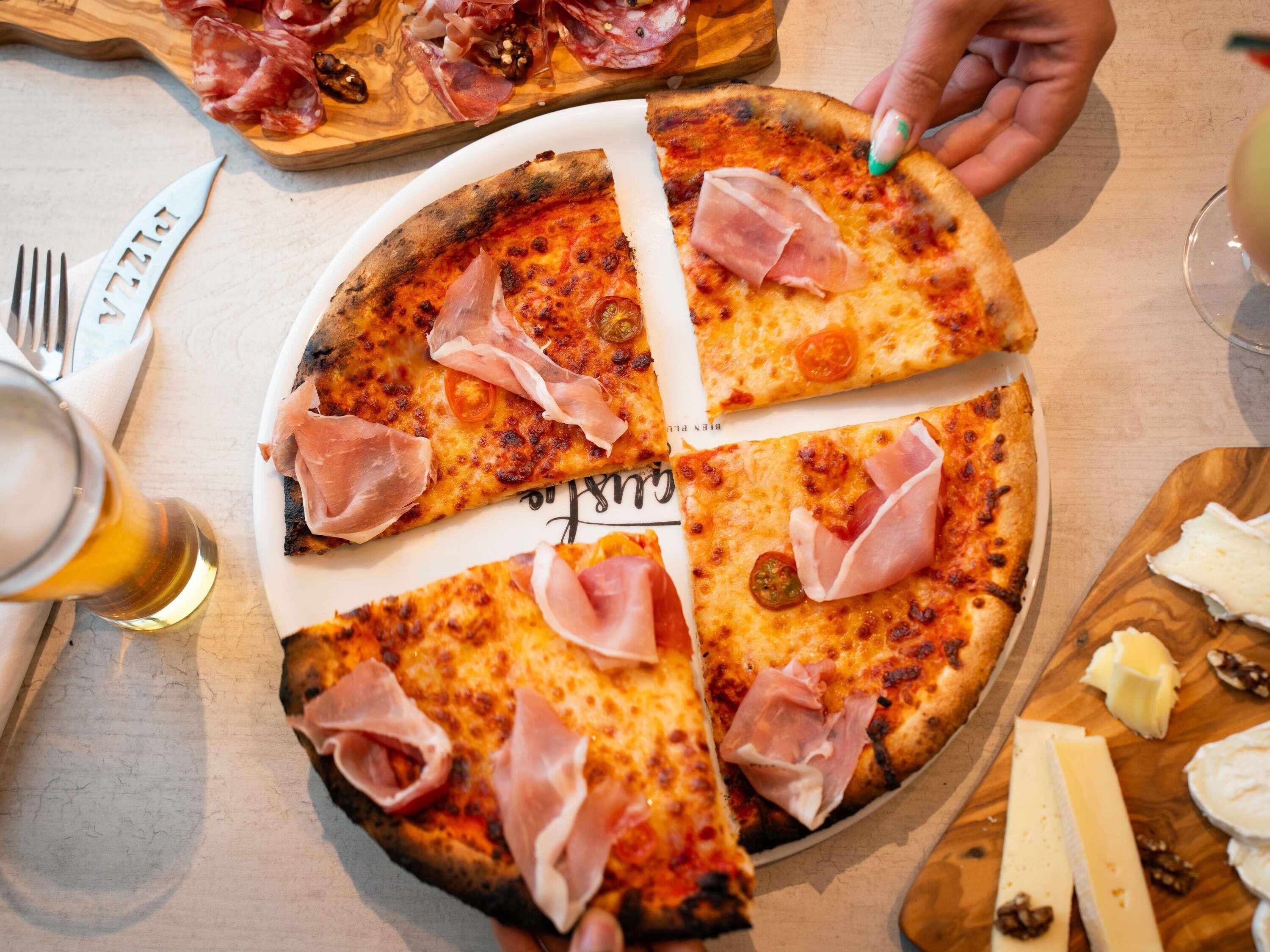 A pizza with slices missing, a fork, a knife, and a glass of beer on a table.