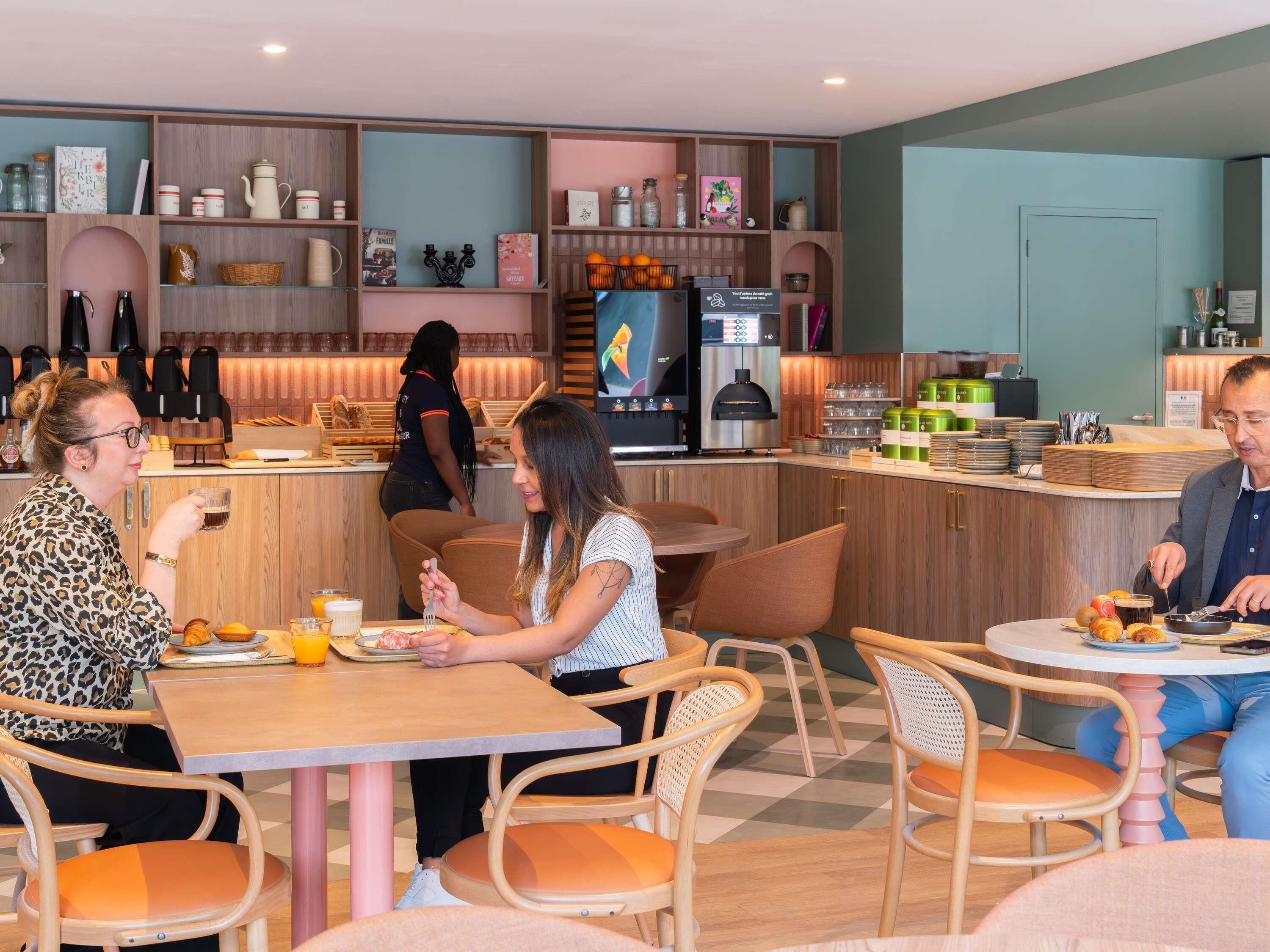 A modern café with wooden furniture, a counter with a coffee machine, and a variety of decorative items on shelves.