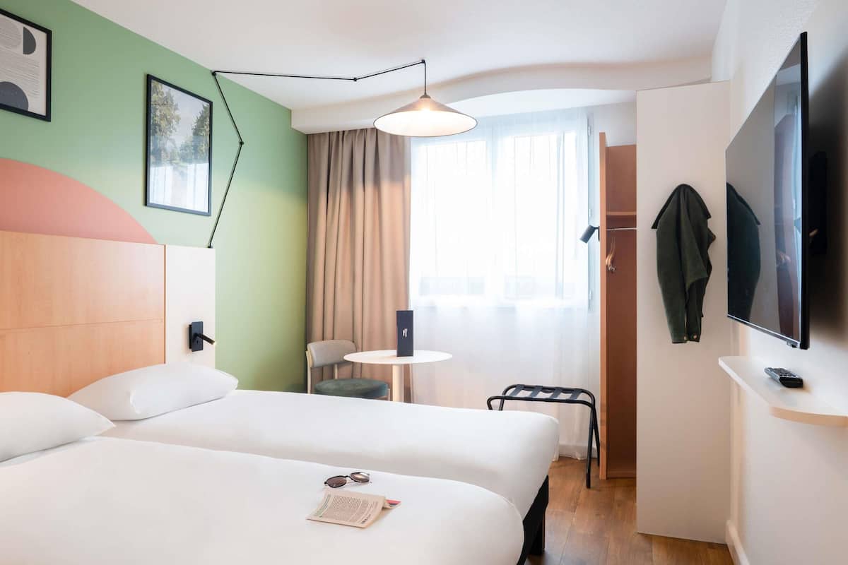 Una habitación de hotel con dos camas, un escritorio con una silla, un televisor y un perchero.