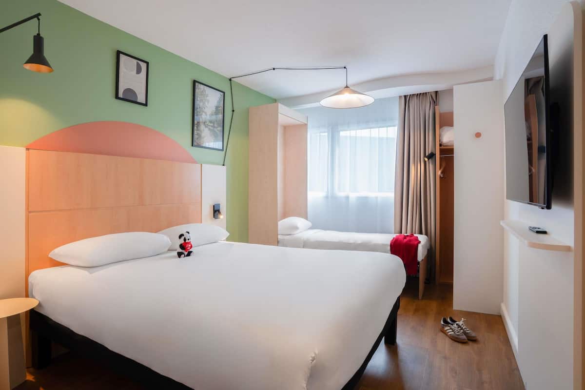 Una habitación de hotel con una cama grande, una mesita de noche, un televisor y un armario.