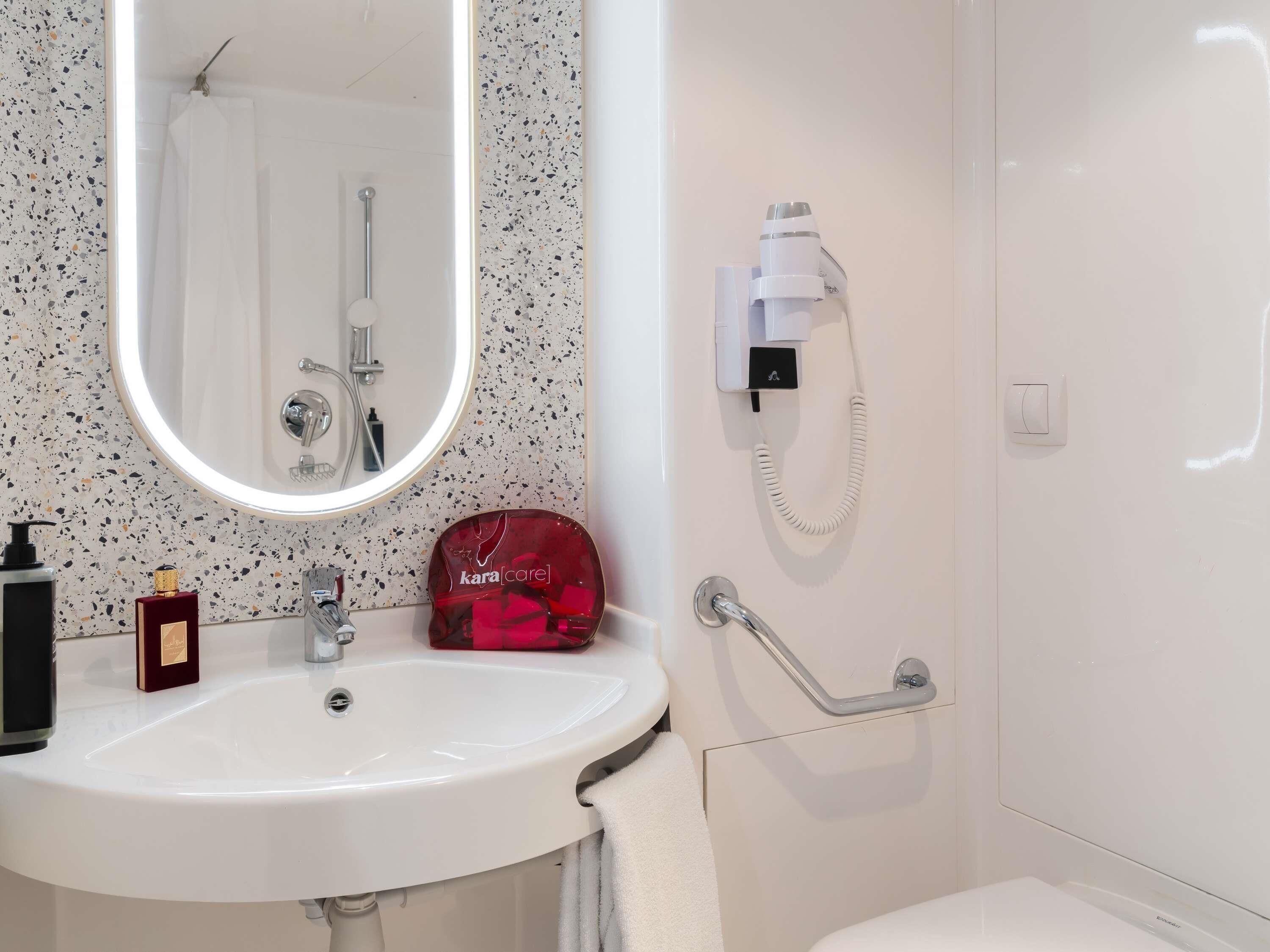 Une salle de bain avec un lavabo blanc, un miroir, une douche et un porte-serviettes.