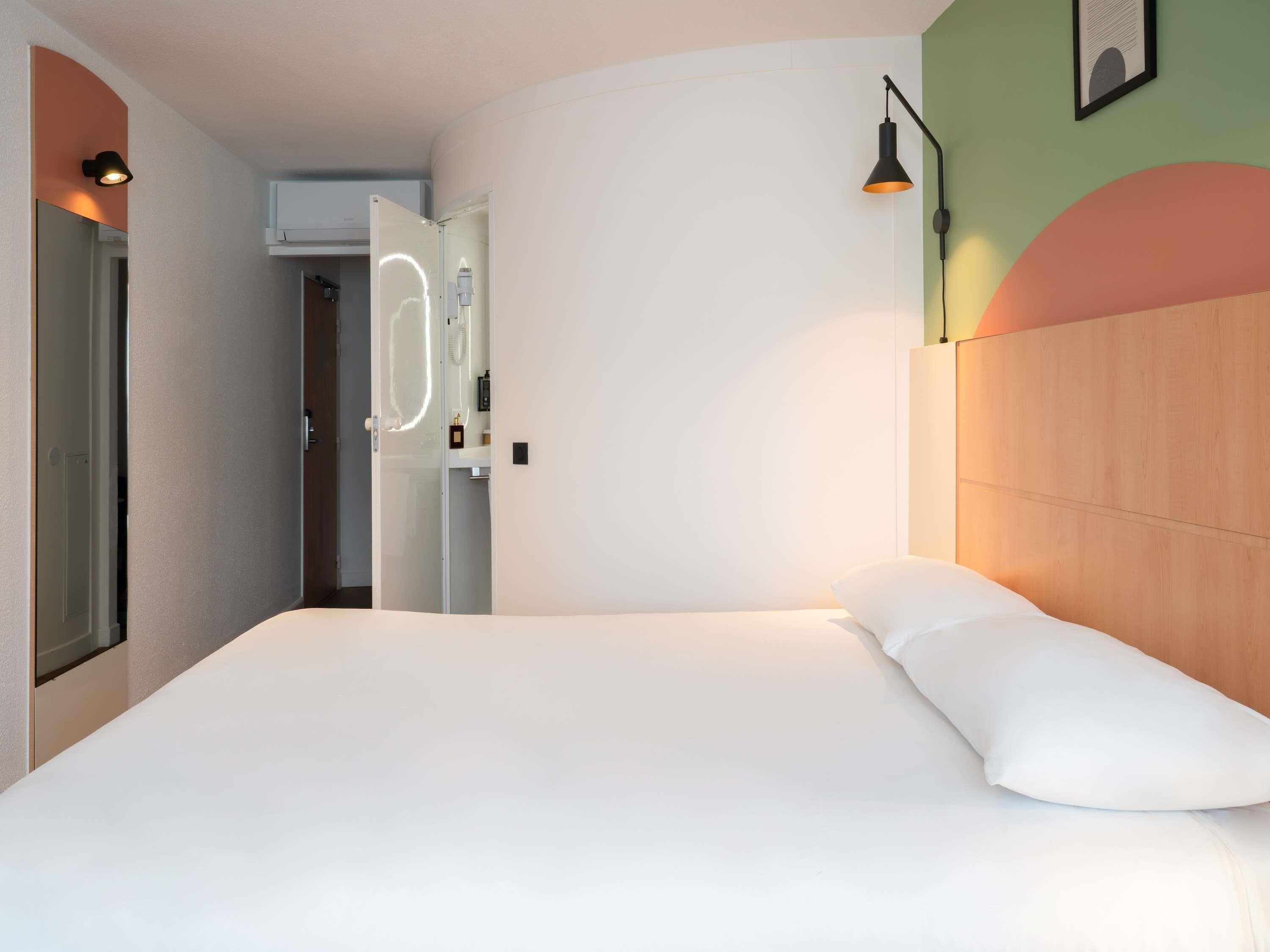 A hotel room with a bed, a door, and a wall-mounted light fixture.